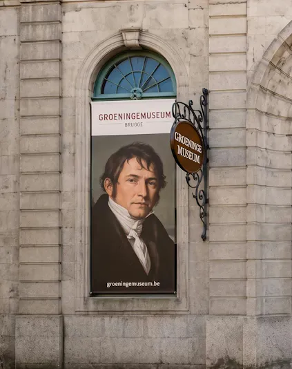 Banner of Groeninge Museum in Brugge with a portrait displayed on a stone building wall.