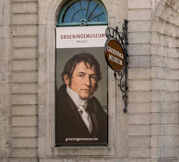 Banner of Groeninge Museum in Brugge with a portrait displayed on a stone building wall.