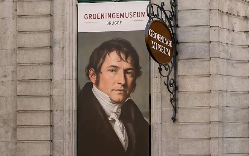Banner of Groeninge Museum in Brugge with a portrait displayed on a stone building wall.