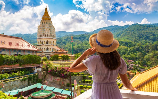 Woman admiring Kek Lok Si Temple with pagoda in Penang, Malaysia, surrounded by lush hills.