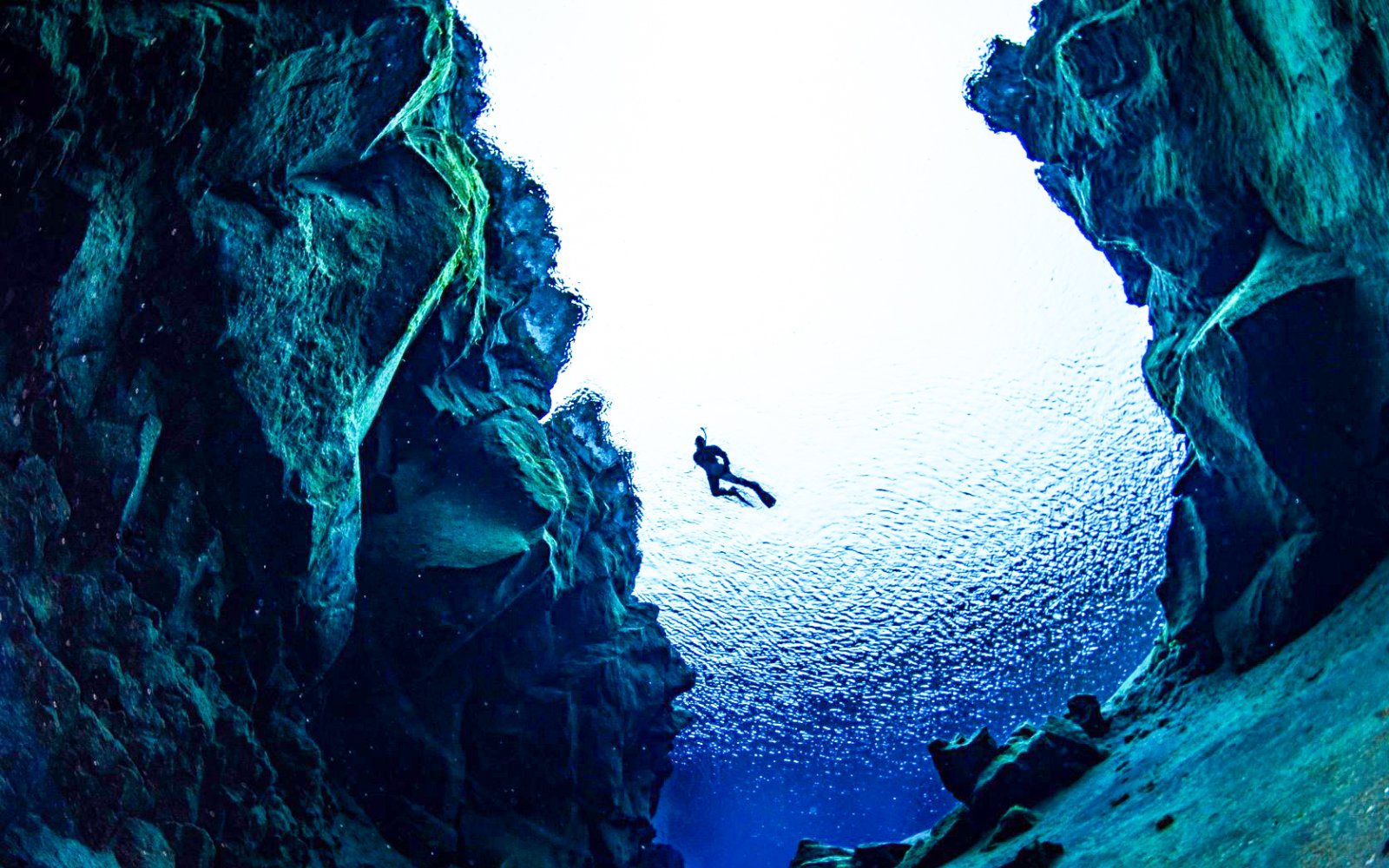 Snorkeler exploring underwater rift between tectonic plates in clear blue water.