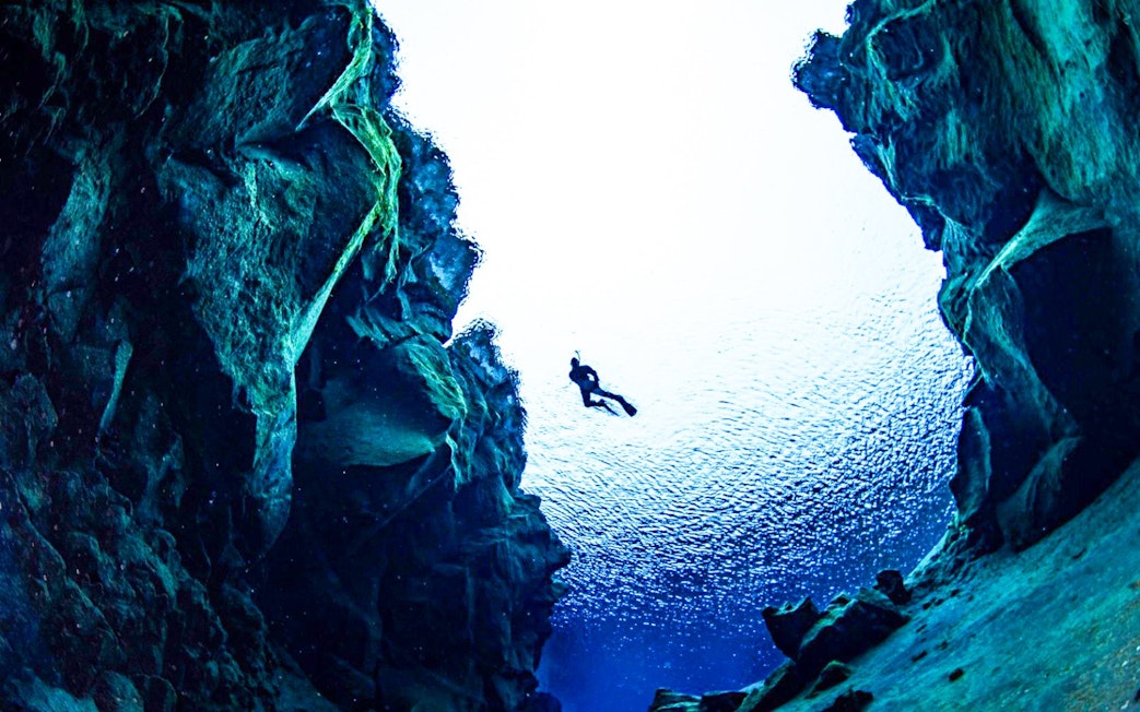 Snorkeler exploring underwater rift between tectonic plates in clear blue water.