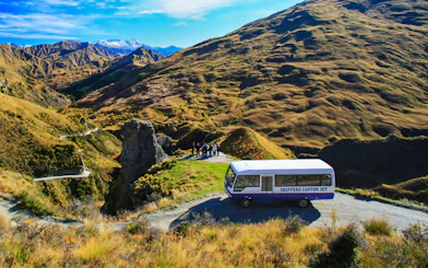 Skippers Canyon Jet bus on a scenic mountain road with guests, New Zealand.