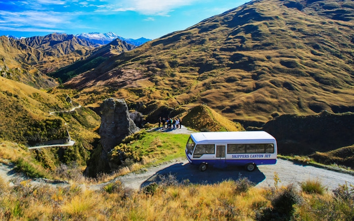 Skippers Canyon Jet bus on a scenic mountain road with guests, New Zealand.