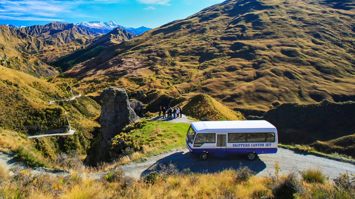 Skippers Canyon Jet bus on a scenic mountain road with guests, New Zealand.