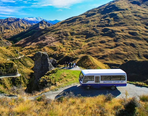 Skippers Canyon Jet bus on a scenic mountain road with guests, New Zealand.