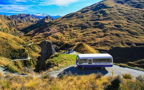 Skippers Canyon Jet bus on a scenic mountain road with guests, New Zealand.