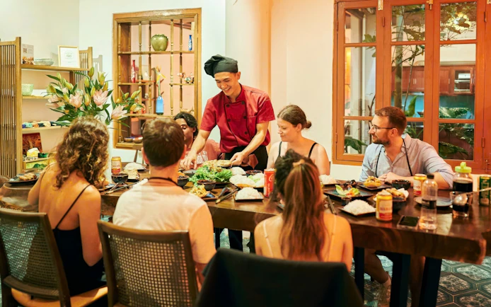 Chef teaching a group at a traditional Vietnamese cooking class in a cozy dining room.