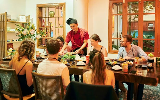 Chef teaching a group at a traditional Vietnamese cooking class in a cozy dining room.