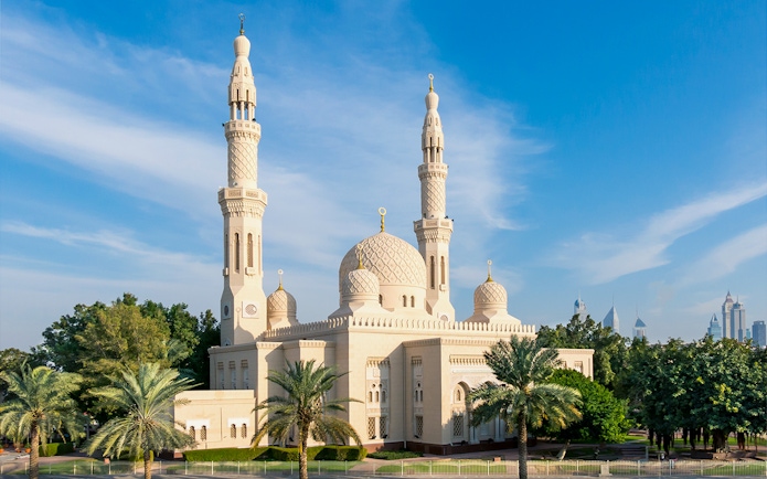 Jumeirah Mosque in Dubai with palm trees and city skyline in the background.