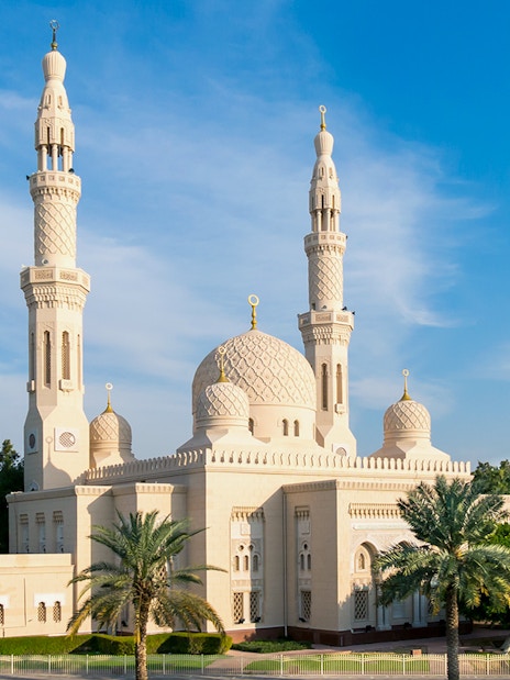 Jumeirah Mosque in Dubai with palm trees and city skyline in the background.