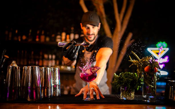 Bartender crafting a vibrant cocktail at Baloo Ibiza bar.