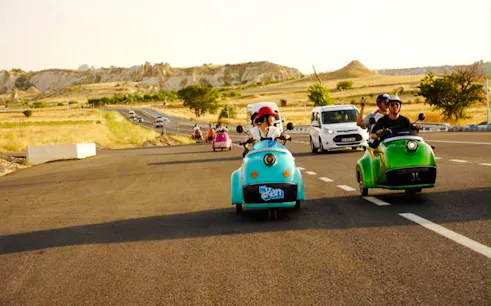 Vintage electric carts on a road in Love Valley, Cappadocia, with scenic rock formations.