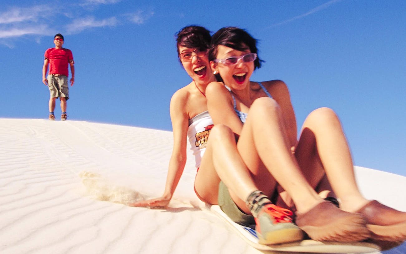 People sandboarding down a dune during a 4WD tour.