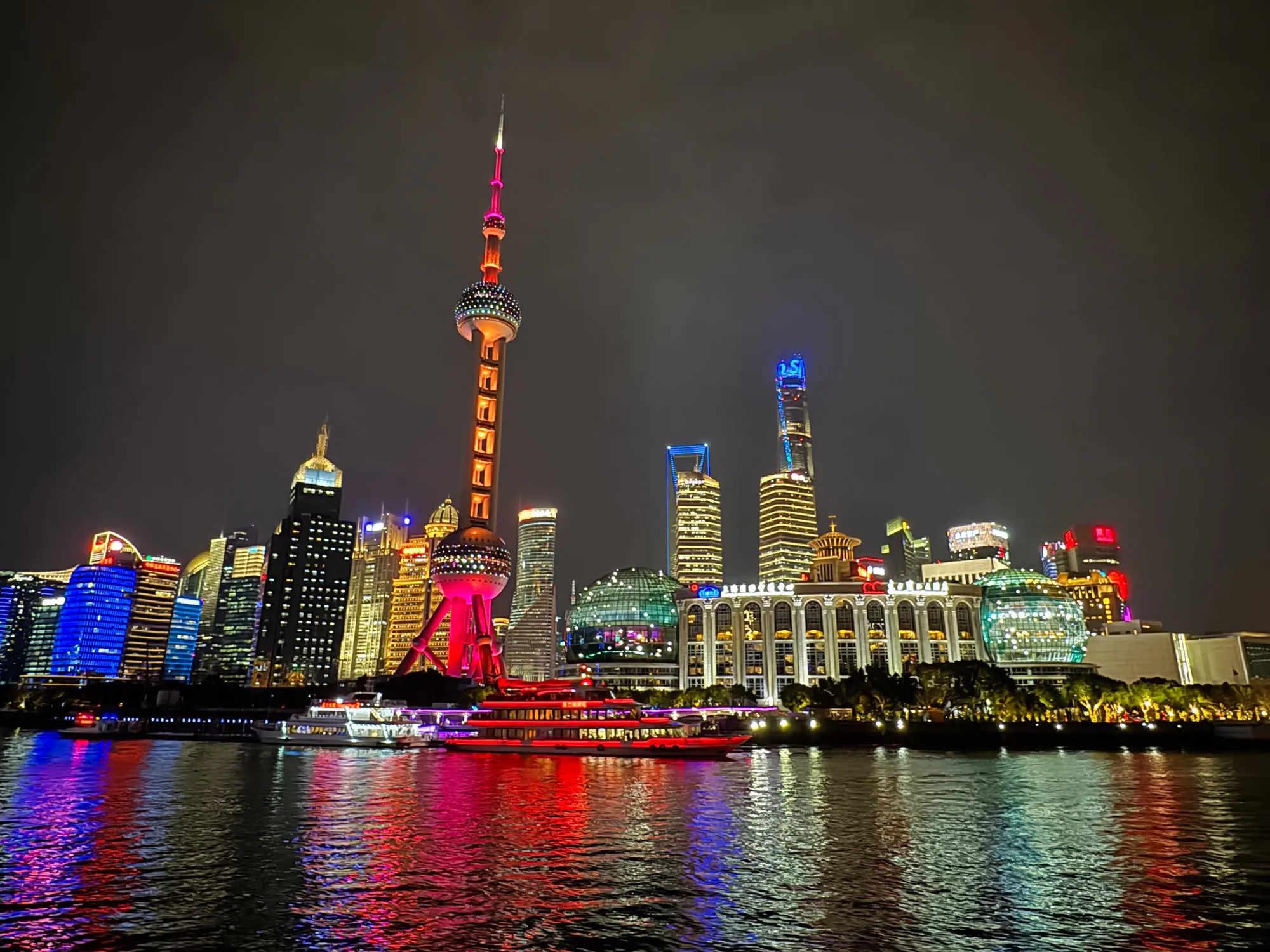 Shanghai Oriental Pearl Tower illuminated at night with city skyline reflections on the Huangpu River.