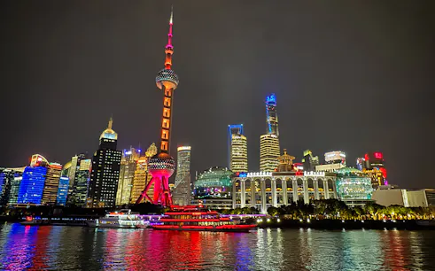 Shanghai Oriental Pearl Tower illuminated at night with city skyline reflections on the Huangpu River.
