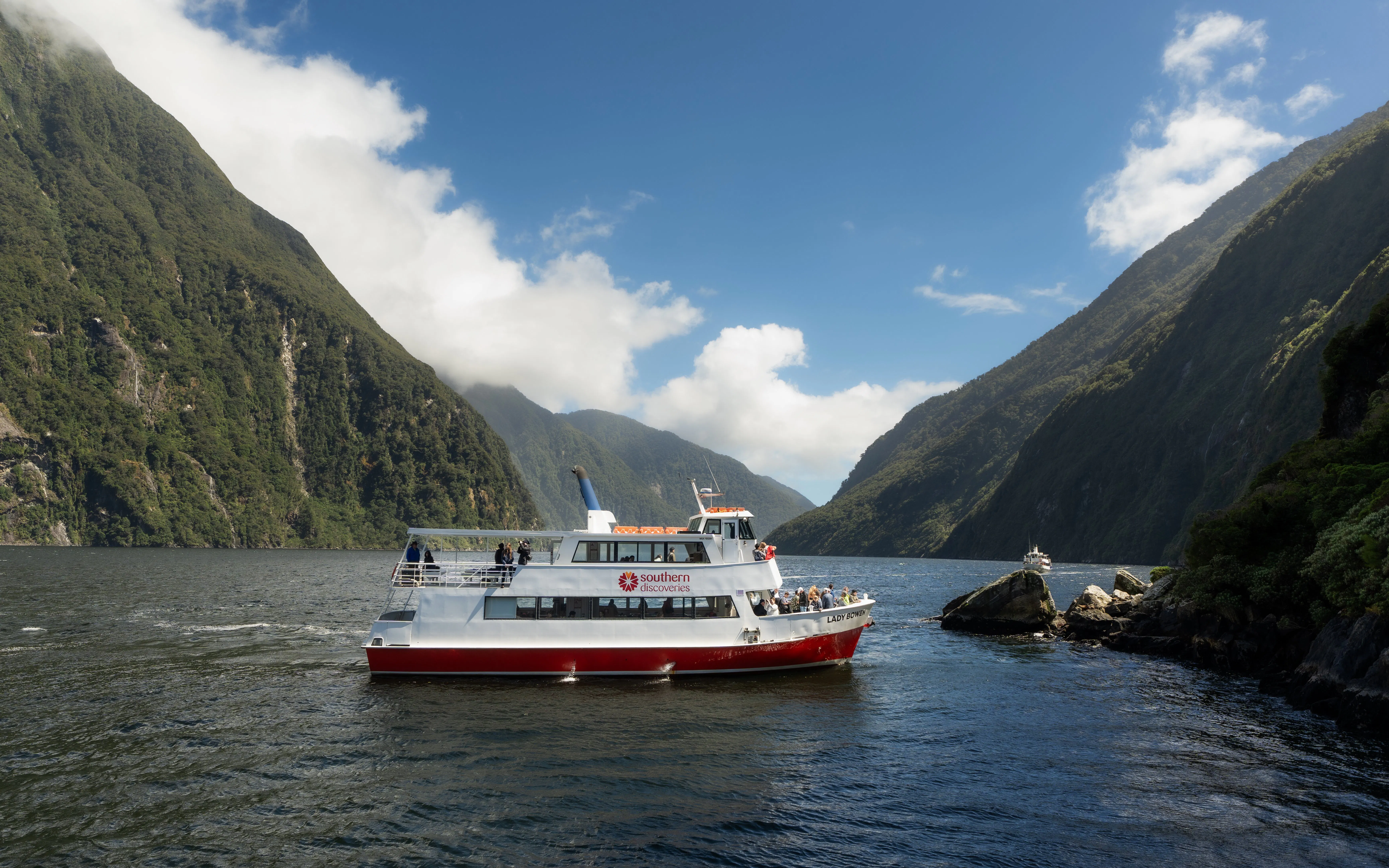Cruise boat navigating Milford Sound fjord with lush mountains in New Zealand.