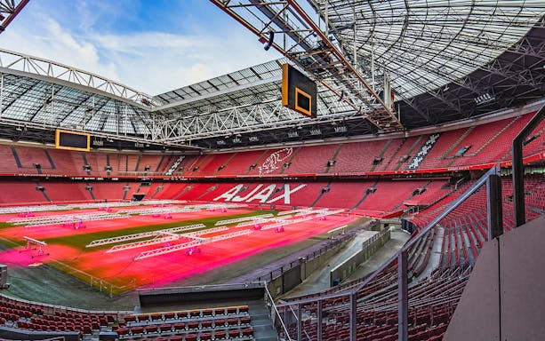 Amsterdam stadium interior with red seats and field lighting setup.