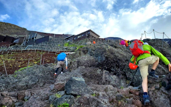 Climbers ascending rocky trail on Mt. Fuji with backpacks.