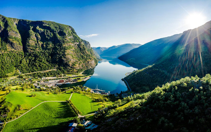 Flam village nestled between mountains and a fjord in Norway, with lush green fields.