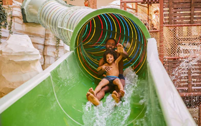 Father and child sliding down a colorful water slide at Bellewaerde Aquapark, Ypres.