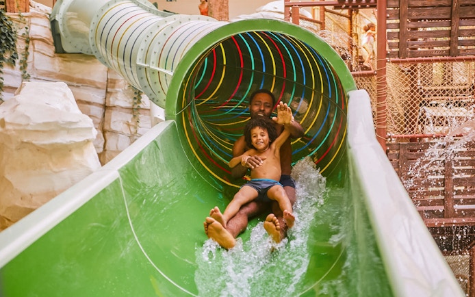 Father and child sliding down a colorful water slide at Bellewaerde Aquapark, Ypres.