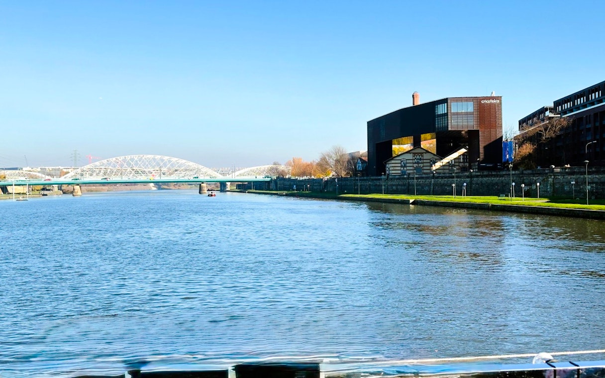 Vistula River in Kraków with Cricoteka and bridge during river cruise.
