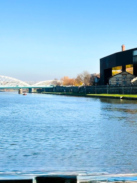 Vistula River in Kraków with Cricoteka and bridge during river cruise.