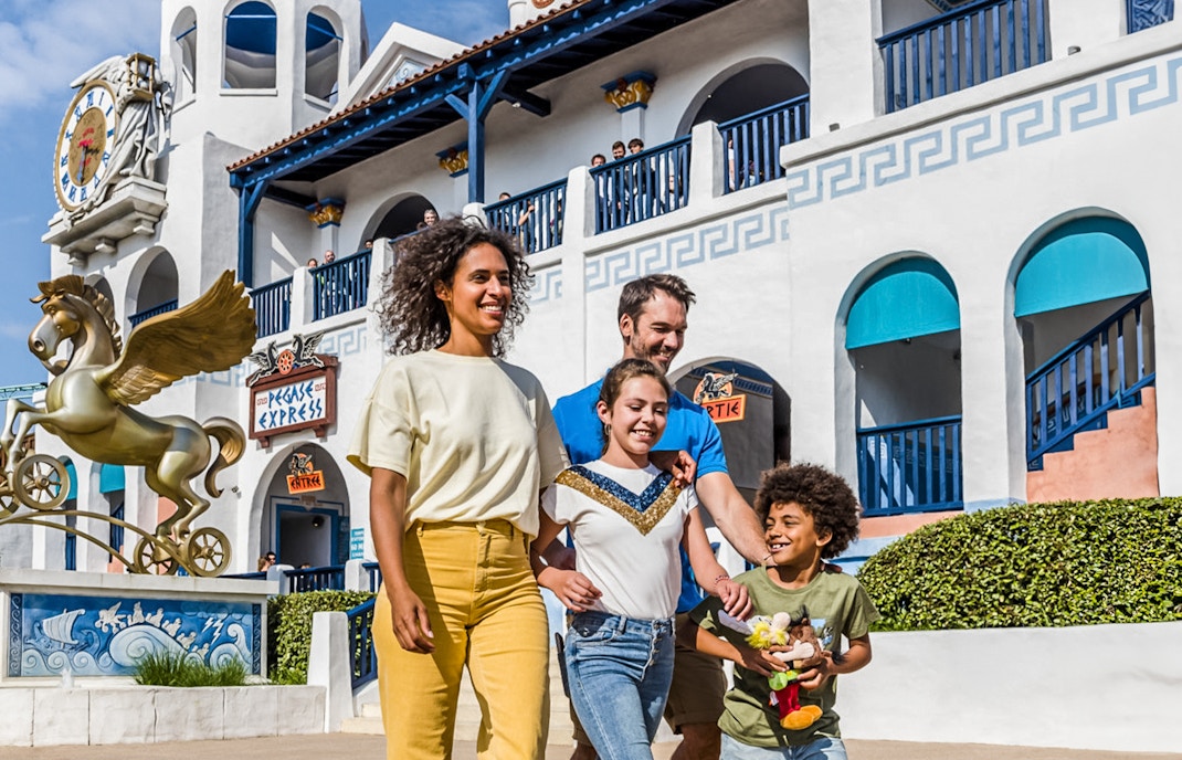 Family walking near Pegasus Express ride at Parc Astérix, France.