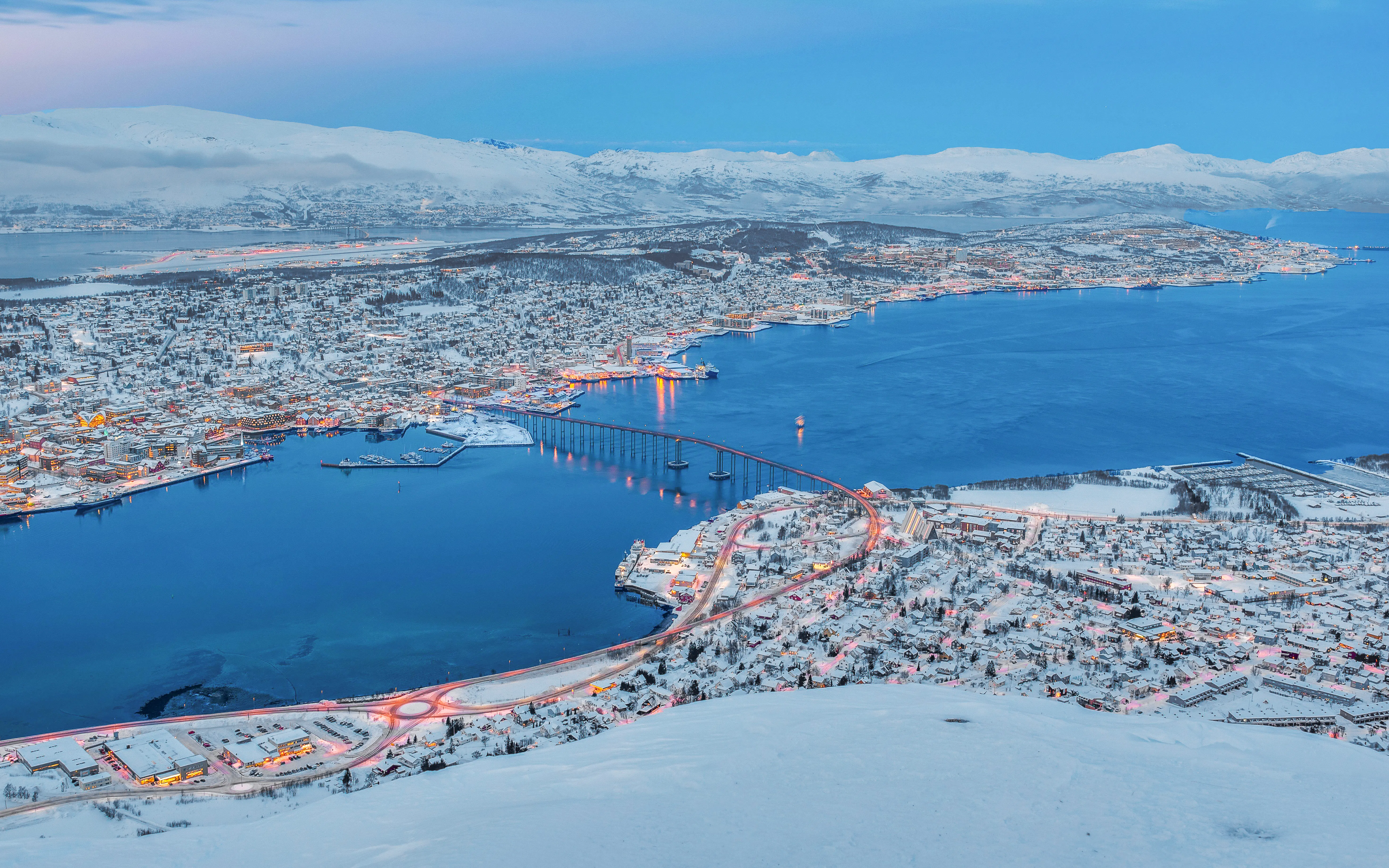 Aerial view of Tromso, Norway, with snow-covered landscape and bridge at sunset in winter.