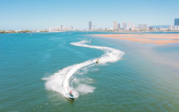 Jet skis creating trails on blue water with city skyline in the background.