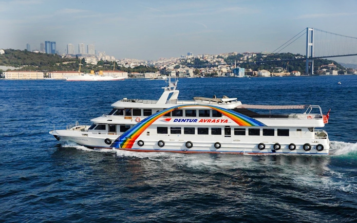Bosphorus cruise ship sailing near Istanbul with cityscape and bridge in the background.