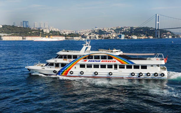 Bosphorus cruise ship sailing near Istanbul with cityscape and bridge in the background.