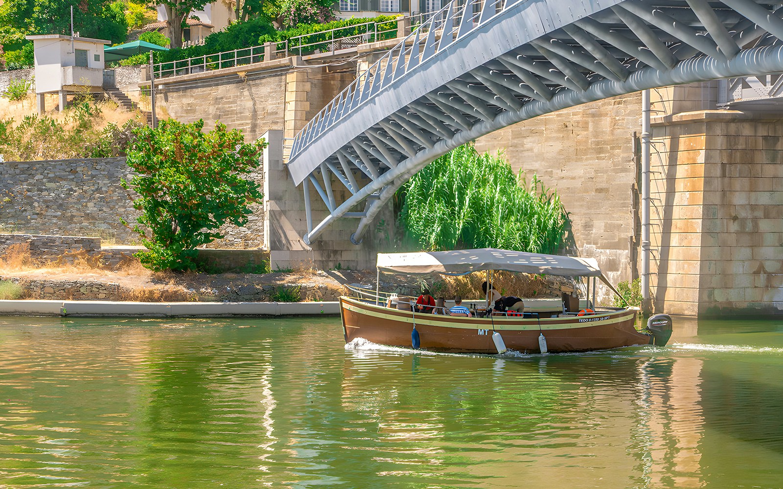 Tourists on a Douro Valley cruise boat passing under a bridge.