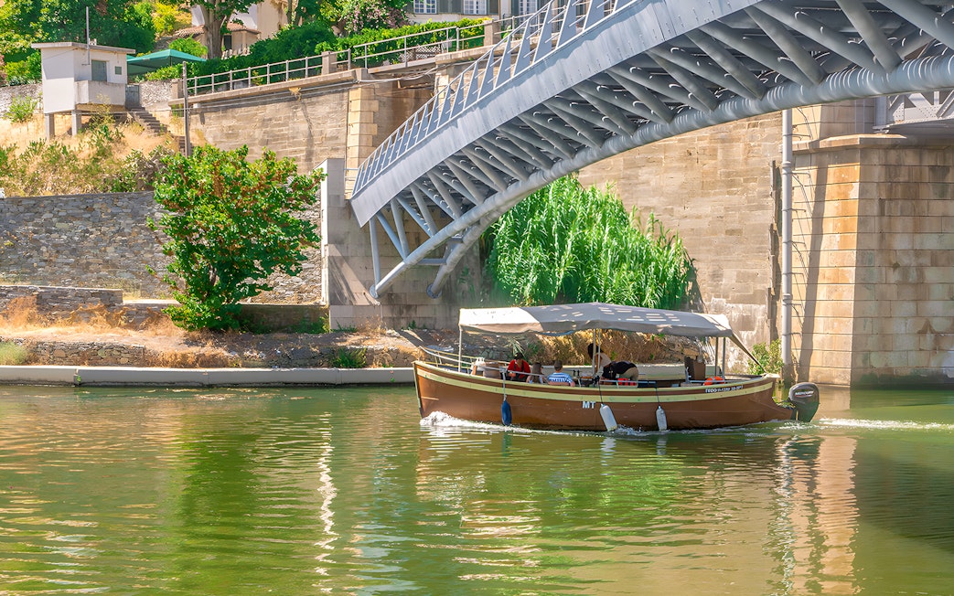 Tourists on a Douro Valley cruise boat passing under a bridge.
