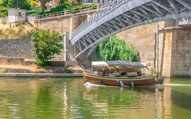 Tourists on a Douro Valley cruise boat passing under a bridge.