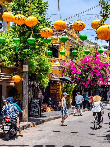 Street view in Hoi An ancient town, Vietnam, with colorful lanterns and vibrant flowers.