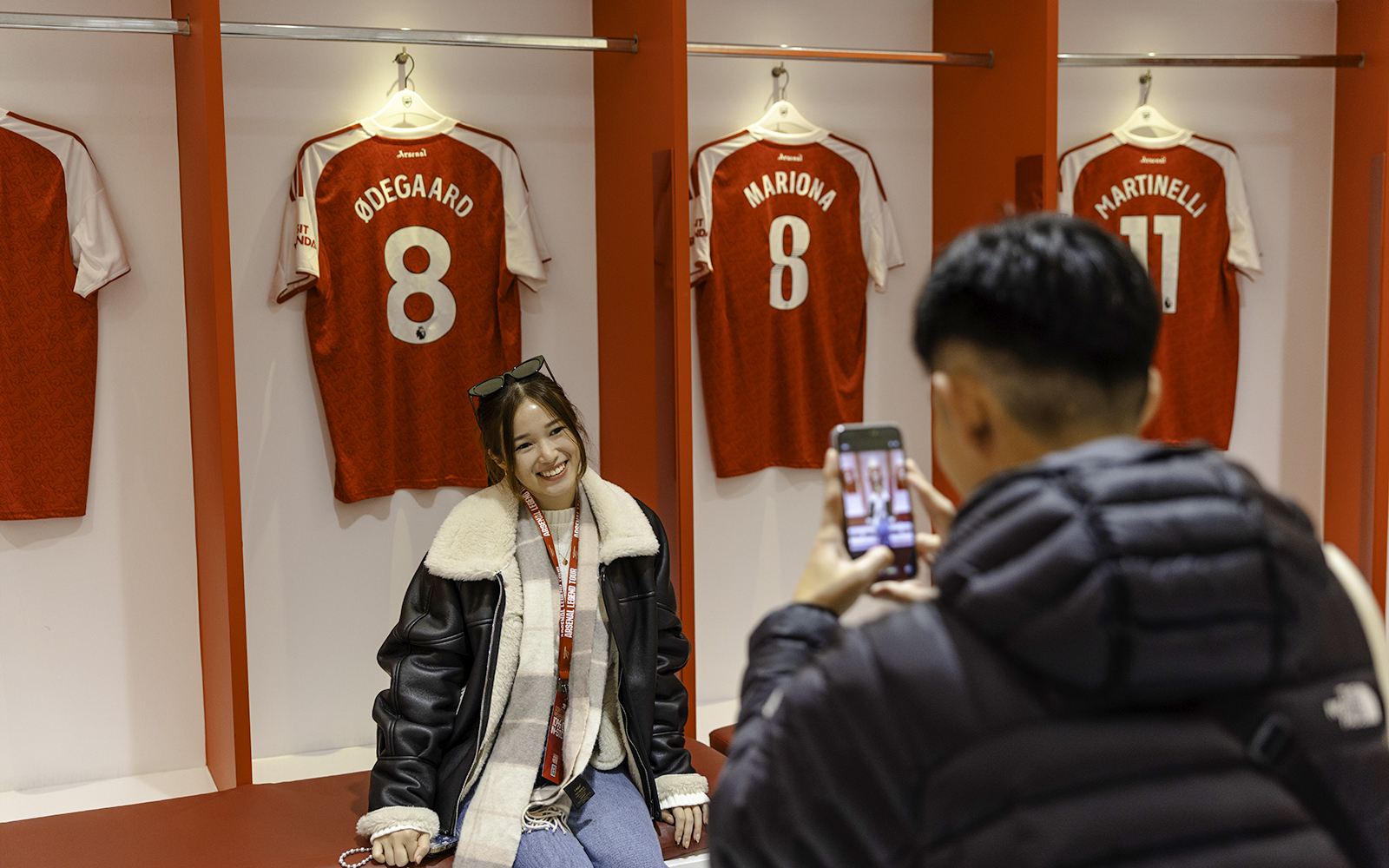 Guests posing in front of player jerseys inside the Emirates Stadium locker room.