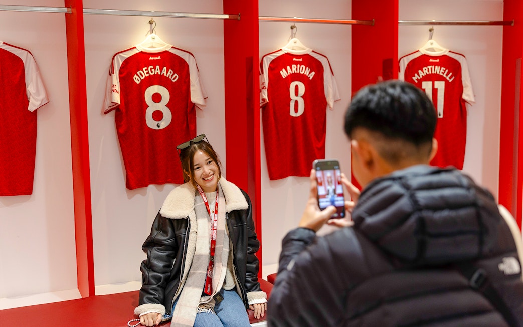 Guests posing in front of player jerseys inside the Emirates Stadium locker room.