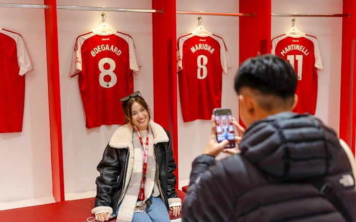 Guests posing in front of player jerseys inside the Emirates Stadium locker room.