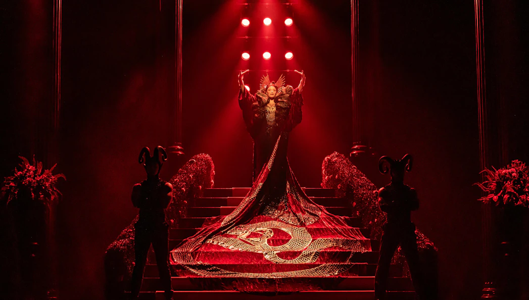 Theatrical scene from The Devil Wears Prada performance in Hamburg with elaborate costume and red lighting.