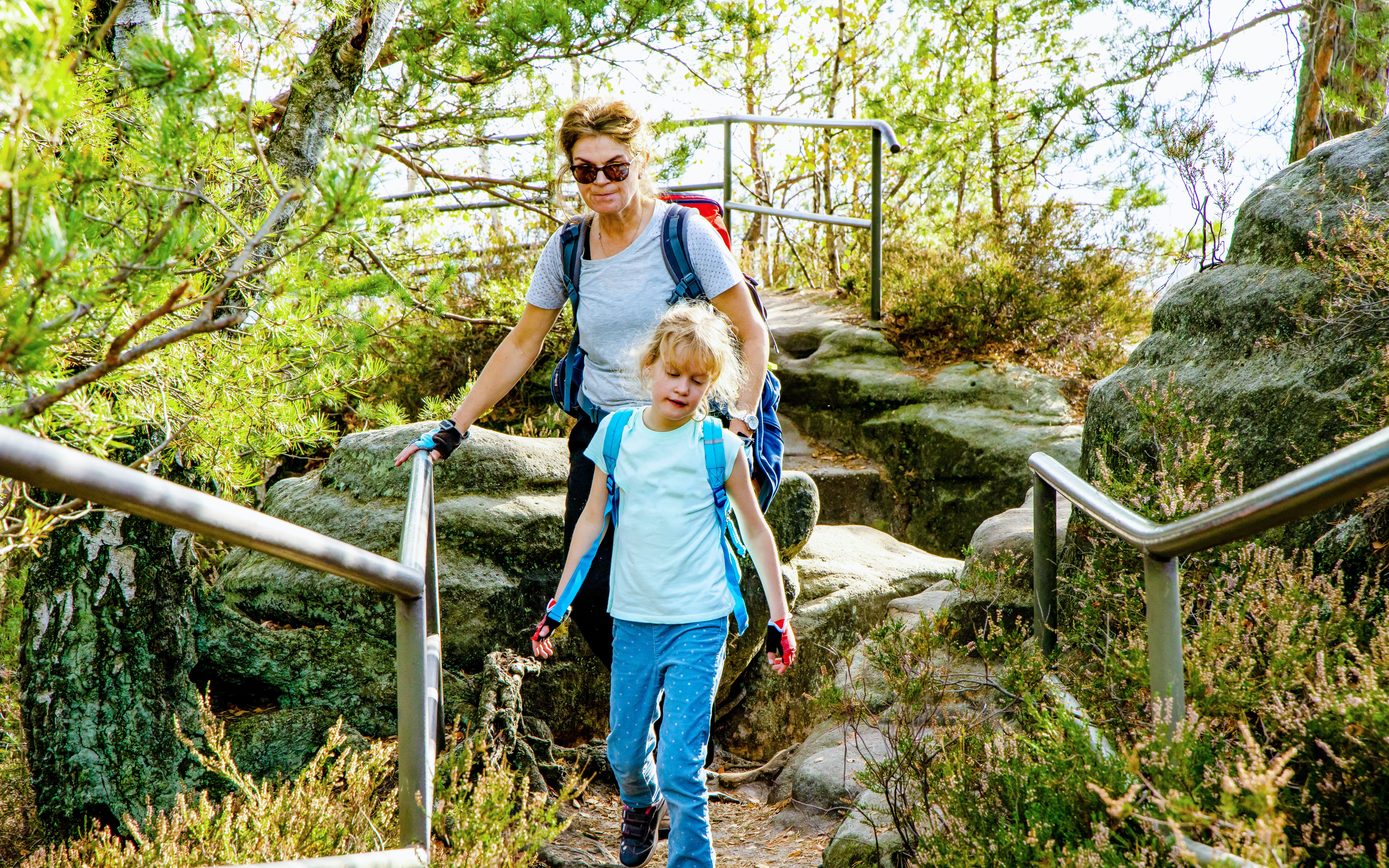 Woman hiking with child on rocky trail in Saxon Switzerland.