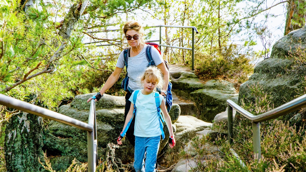 Woman hiking with child on rocky trail in Saxon Switzerland.