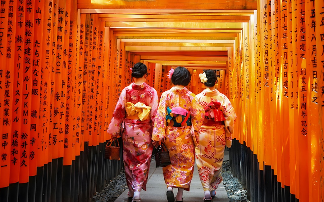 Women in kimonos walking through Fushimi Inari Shrine's torii gates in Kyoto.