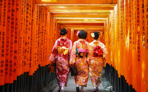 Women in kimonos walking through Fushimi Inari Shrine's torii gates in Kyoto.