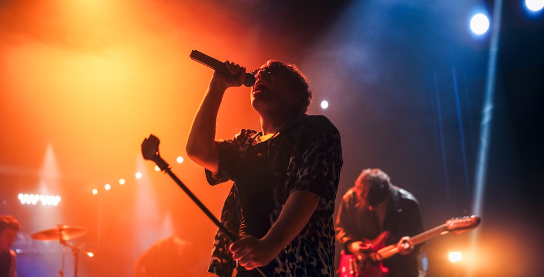 Lead singer performing on stage with band under vibrant stage lights.
