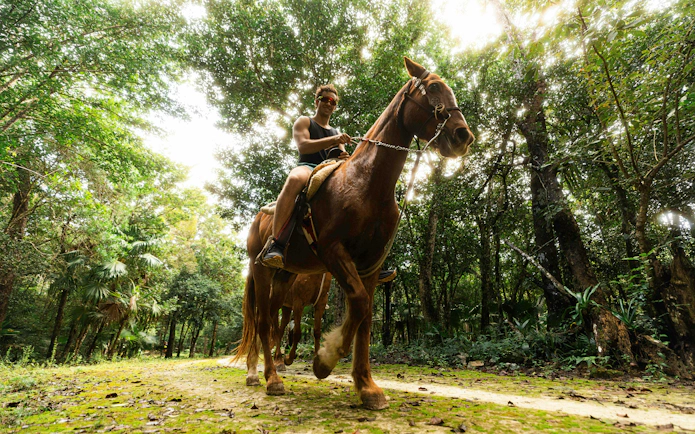 Horseback riding through lush forest at Cancun Extreme Adventuring Park.