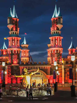 Vialand Theme Park entrance with illuminated castle towers and a golden statue at night.