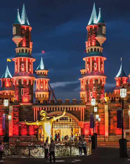 Vialand Theme Park entrance with illuminated castle towers and a golden statue at night.