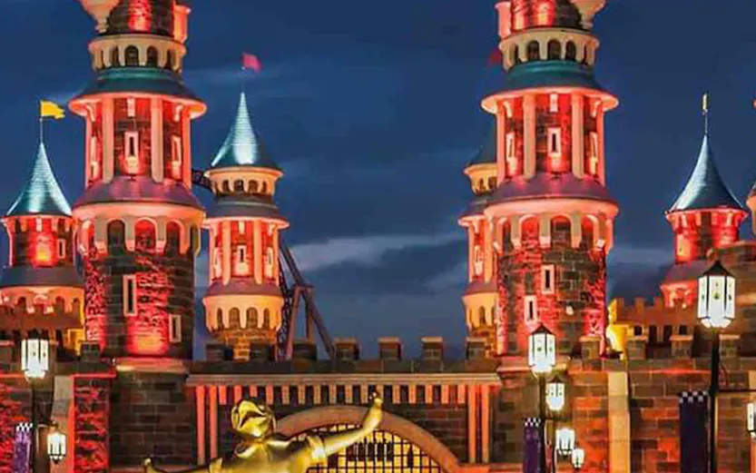 Vialand Theme Park entrance with illuminated castle towers and a golden statue at night.